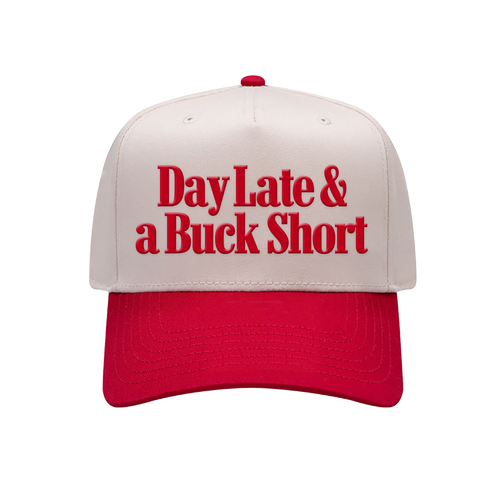 A structured baseball cap with an off-white crown and a bright red brim, featuring the phrase 'Day Late & a Buck Short' embroidered in red across the front panels.